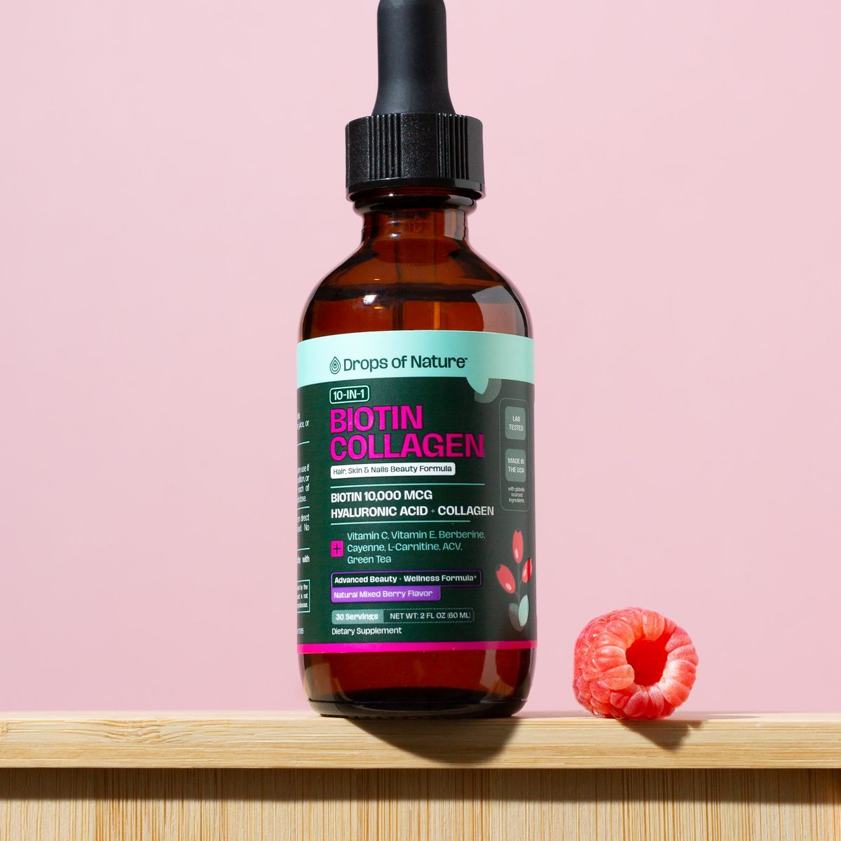 Drops of Nature 10-in-1 Biotin Collagen bottle on a shelf with fresh raspberries.