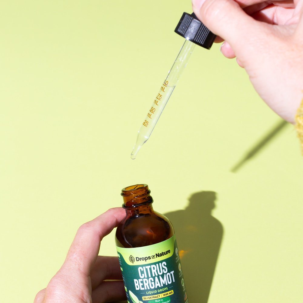 A hand holding a bottle of Citrus Bergamot drops.