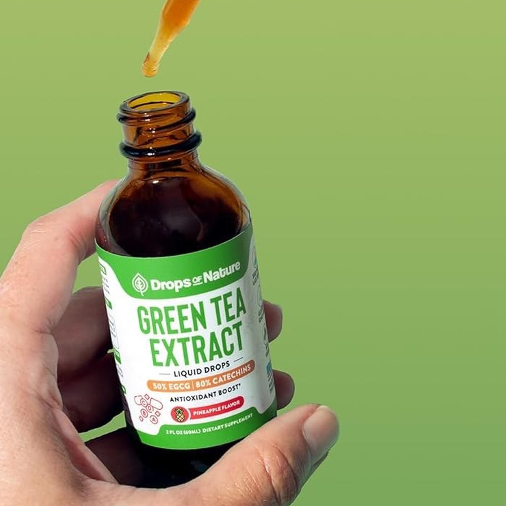 A hand holding a bottle of Green Tea Extract drops.