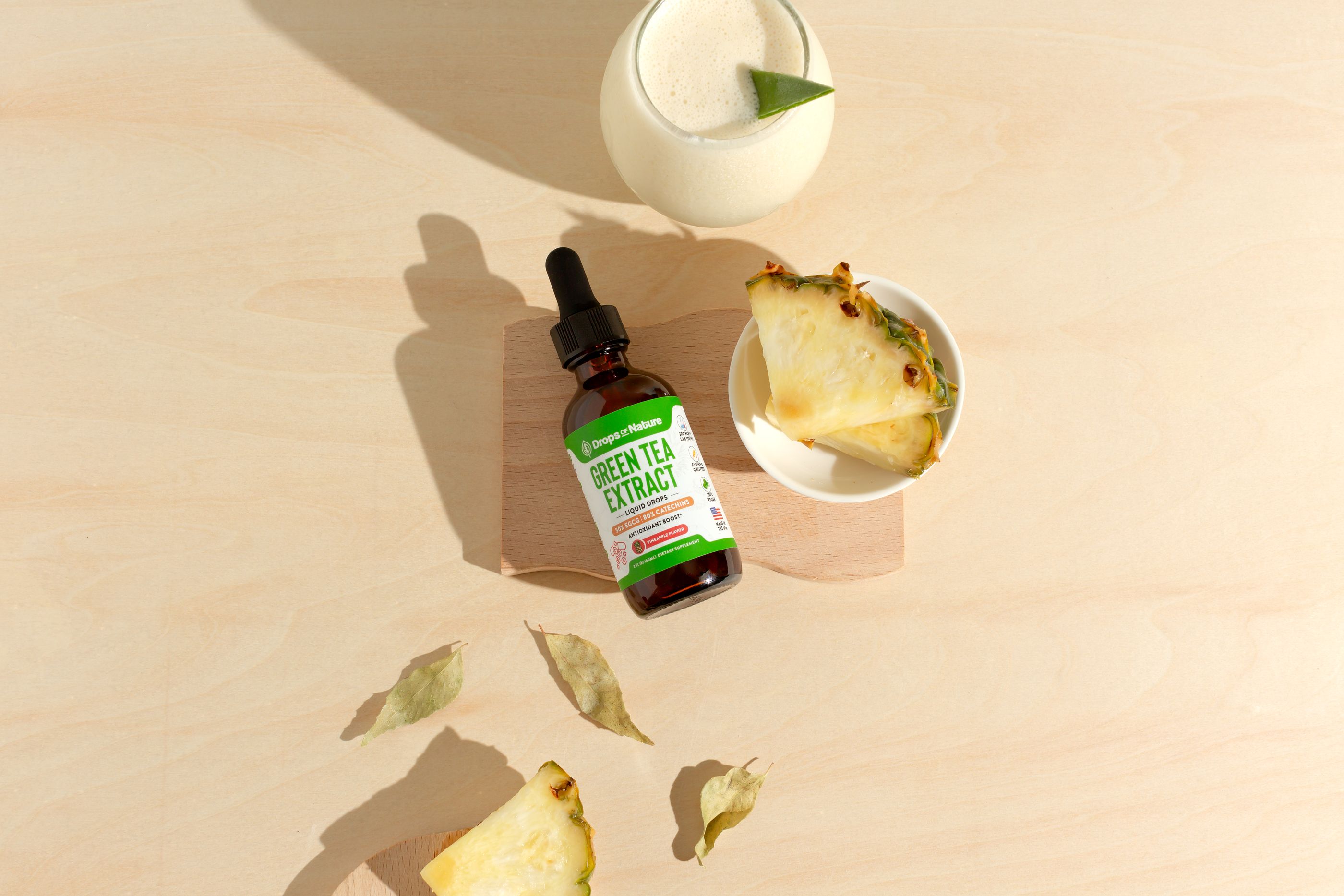 A bottle of Drops of Nature Green Tea Extract liquid drops on light wood with fresh pineapple