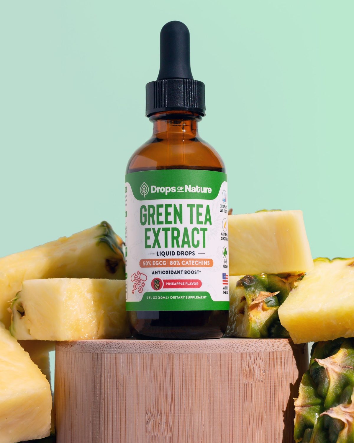 Drops of Nature Green Tea Extract liquid drops on a wooden block beside a pineapple