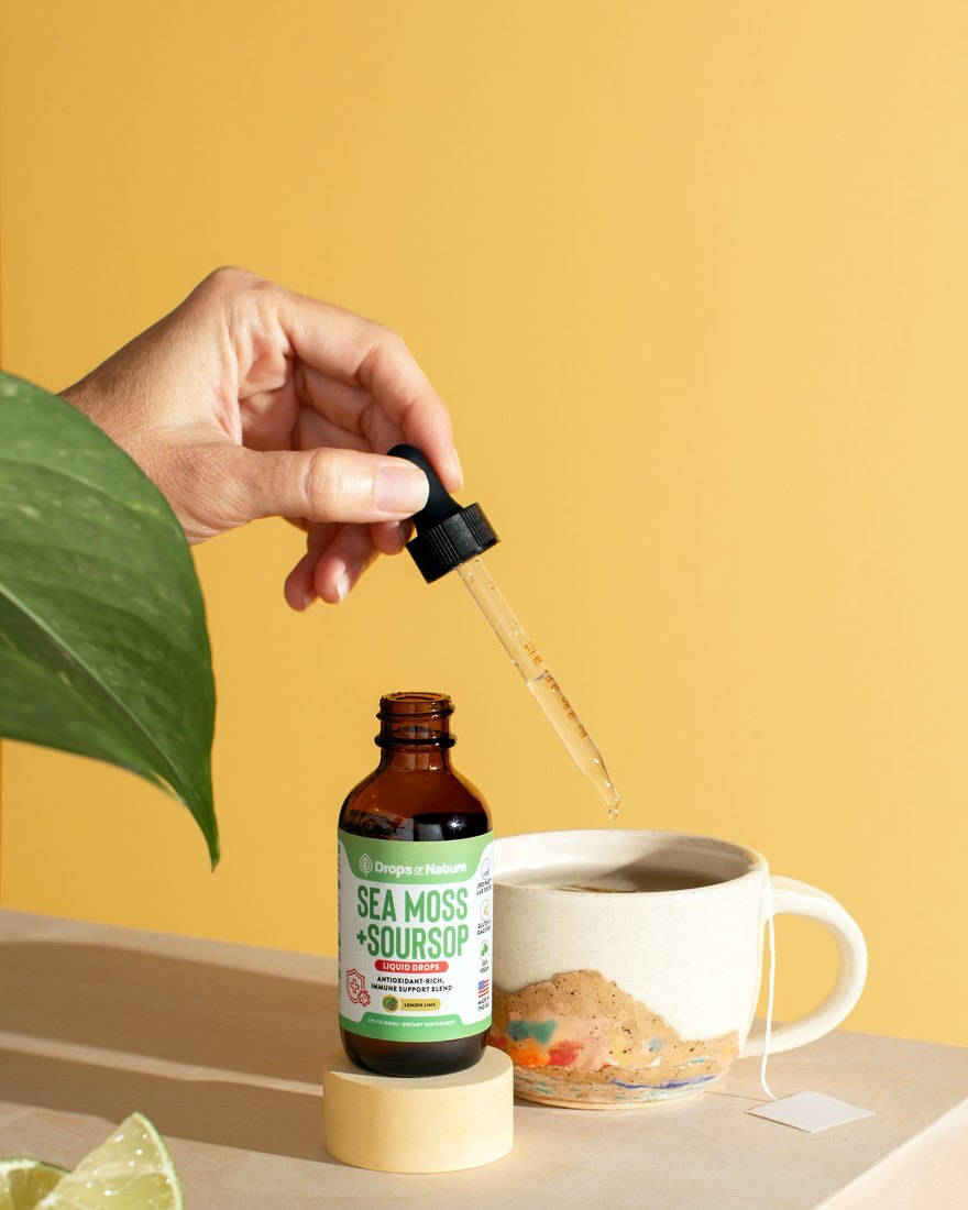Soursop + Sea Moss drops beside a mug of tea with lemon