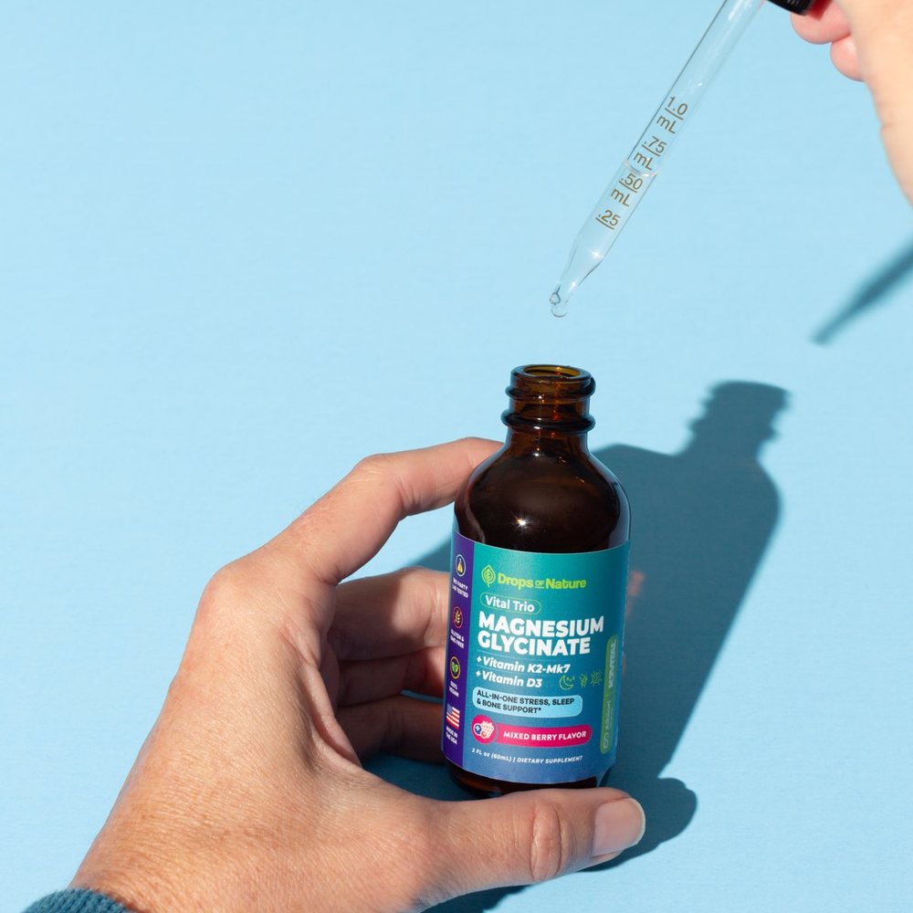 A hand holding a bottle of Magnesium + D3 & K2 drops.