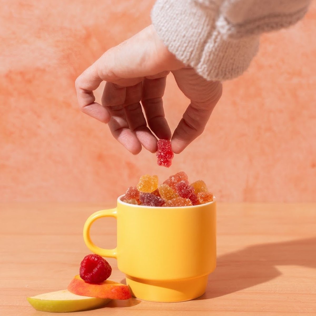 A hand dropping Drops of Nature mushroom gummies into a yellow mug