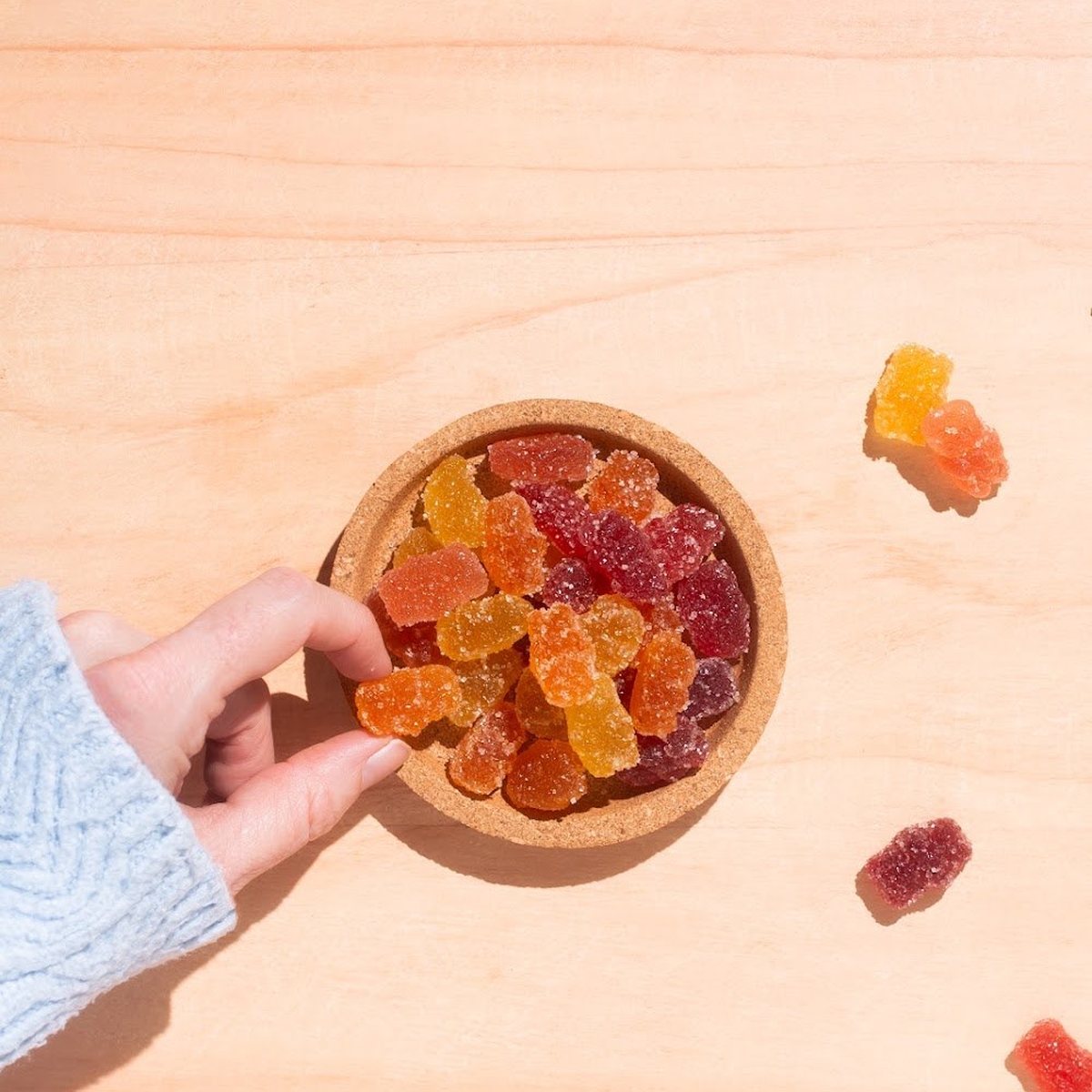 A hand holding a bowl of mixed fruit gummy bears.