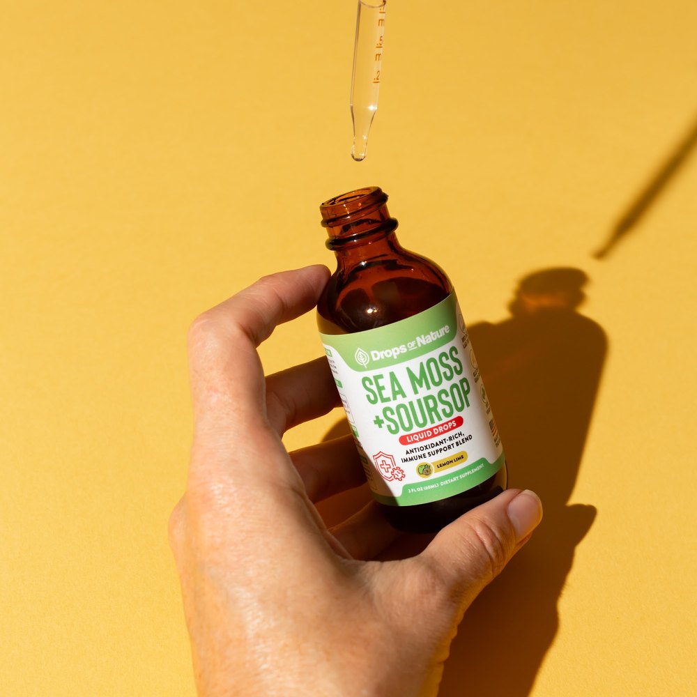 A hand holding a bottle of Soursop + Sea Moss drops.
