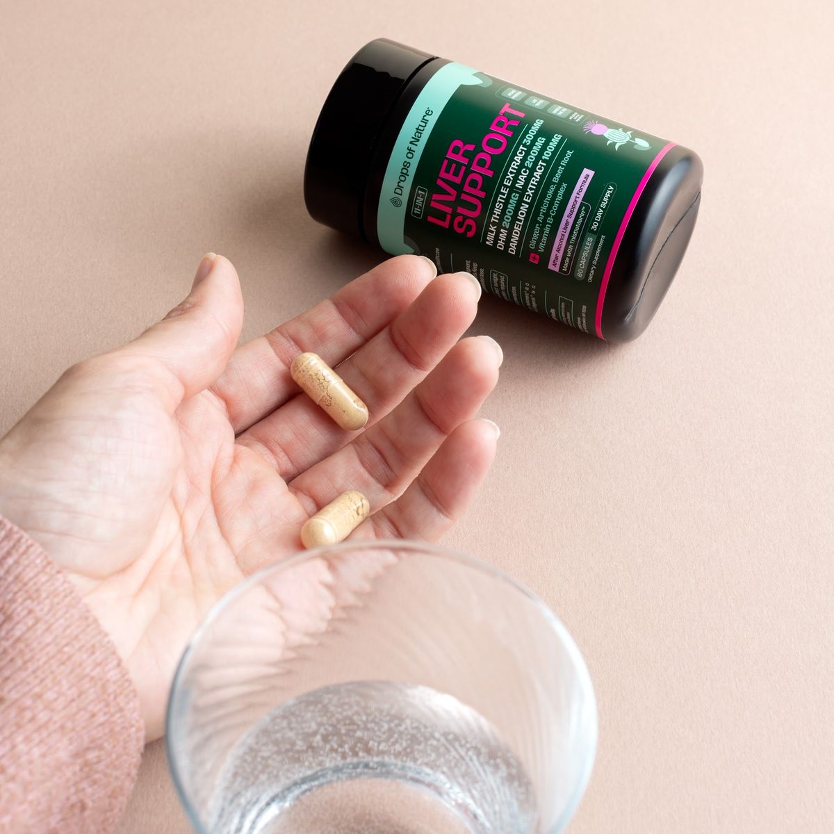 Liver Support capsules in a palm next to the bottle and a glass of water.