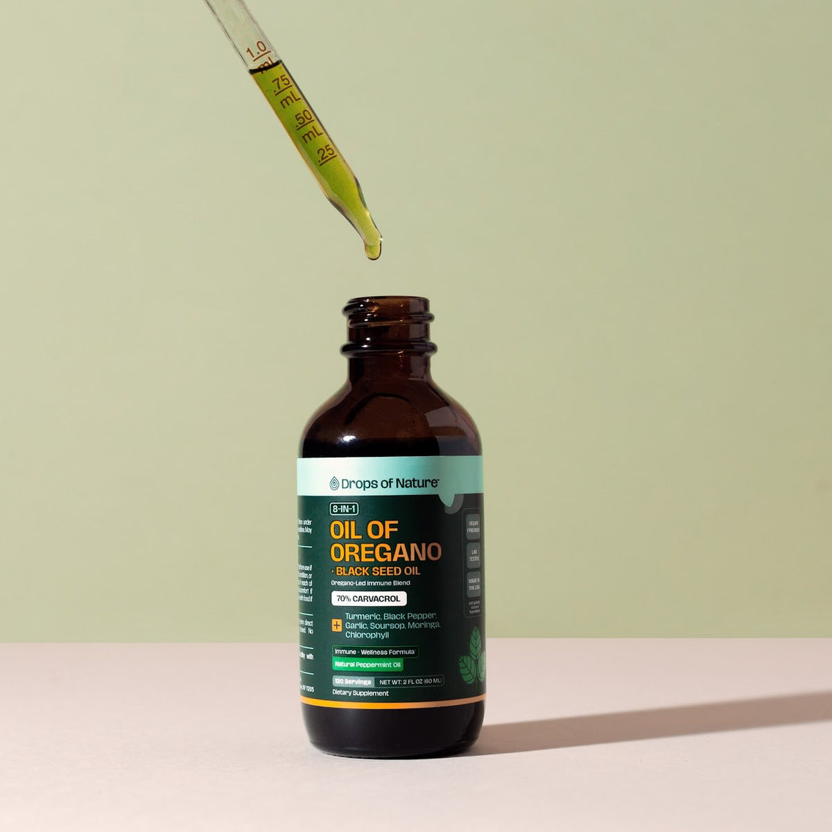 A dropper of green oregano oil over the open bottle.