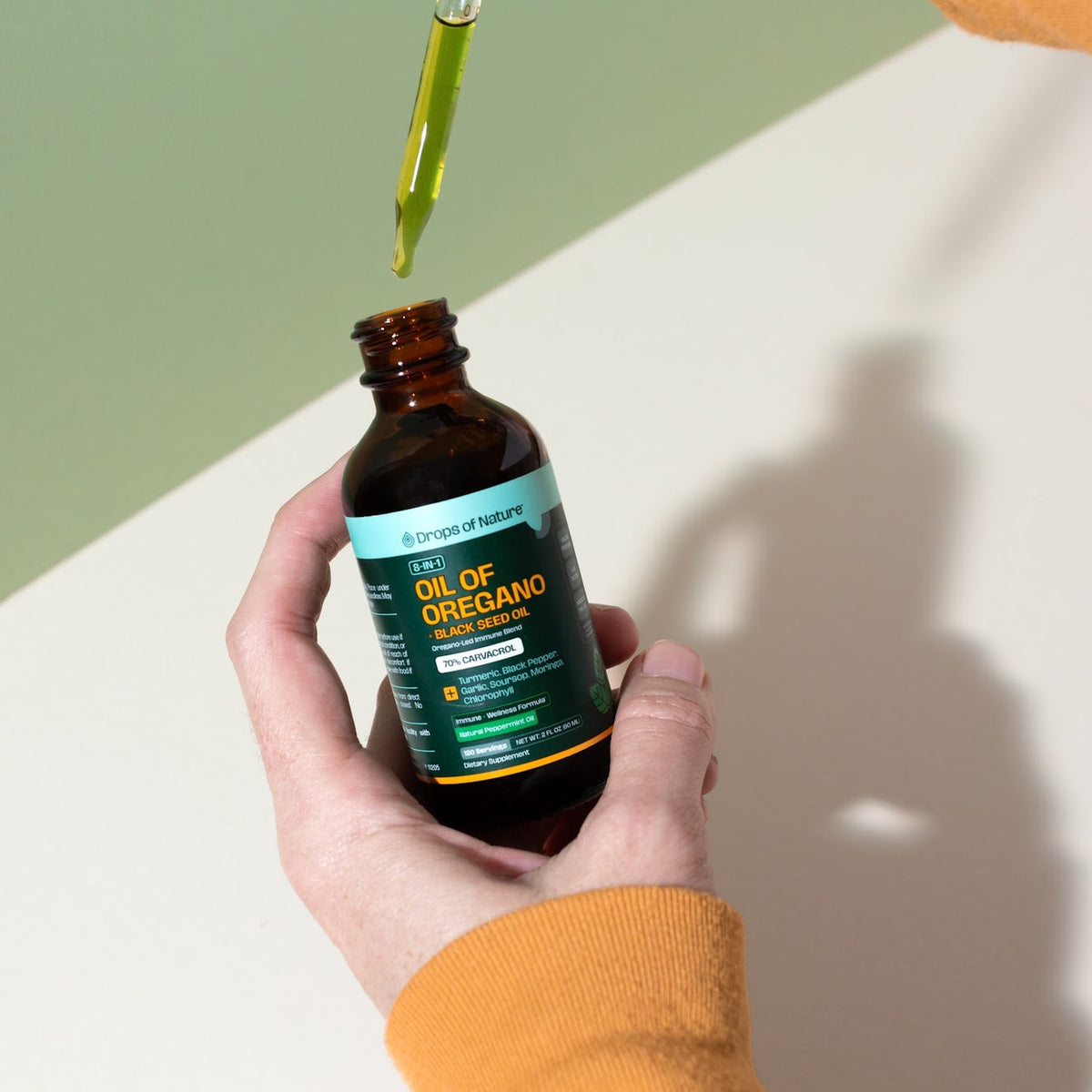 Hand holding the Oil of Oregano bottle with the dropper above it.