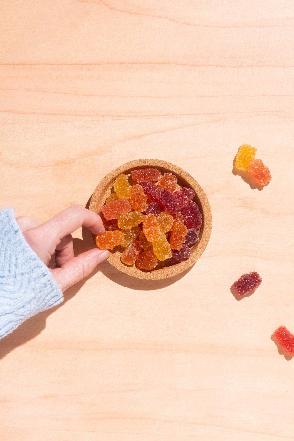 A hand taking a gummy from a bowl of mixed fruit gummies