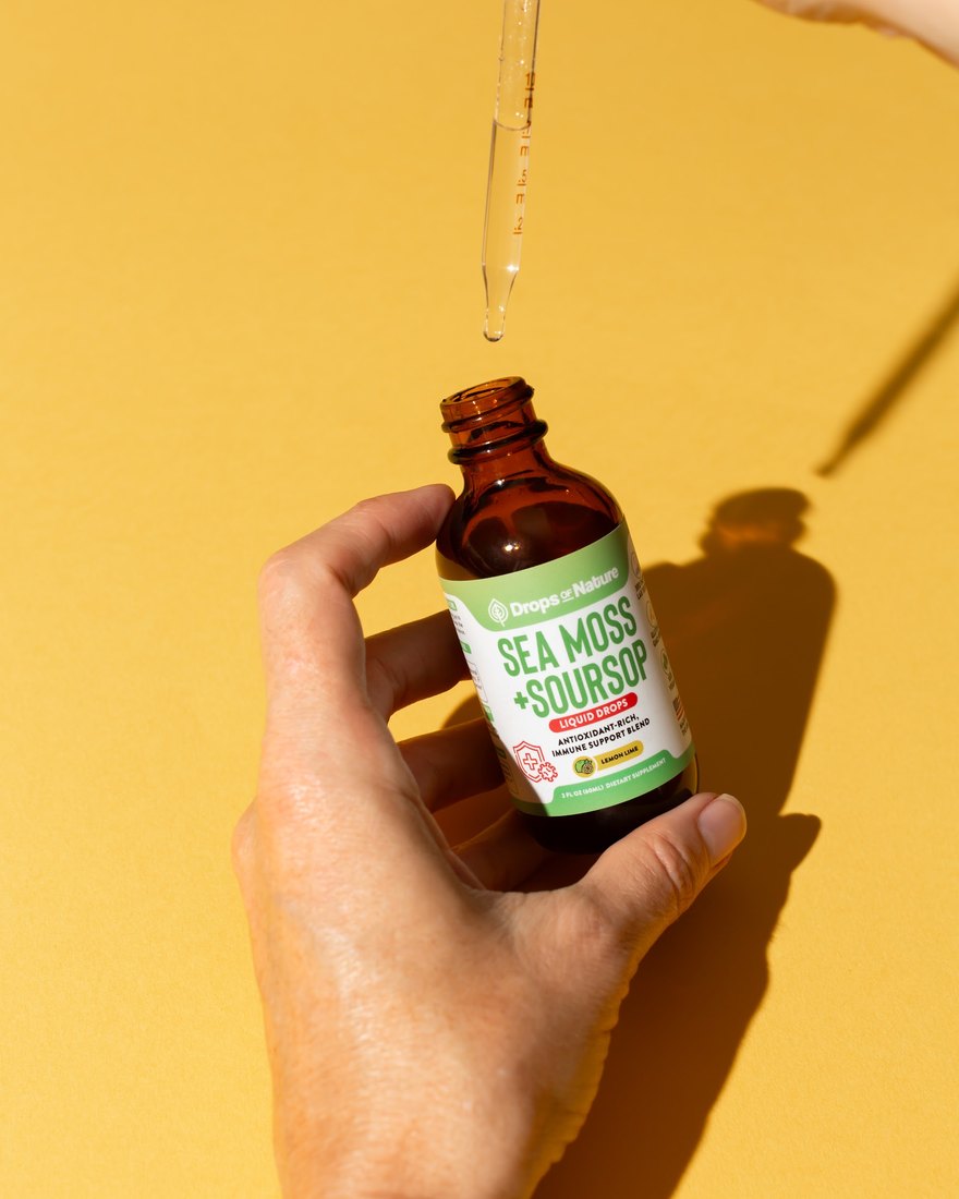 A hand holding a bottle of Soursop + Sea Moss drops