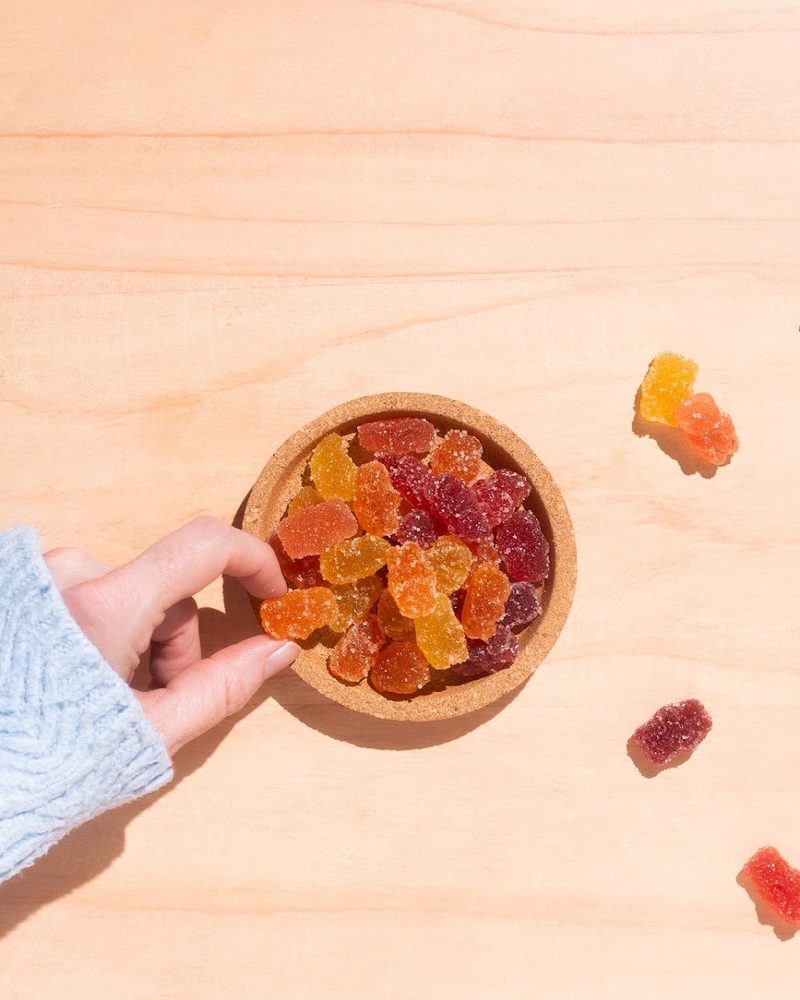 A hand holding a bowl of mixed fruit mushroom gummy bears