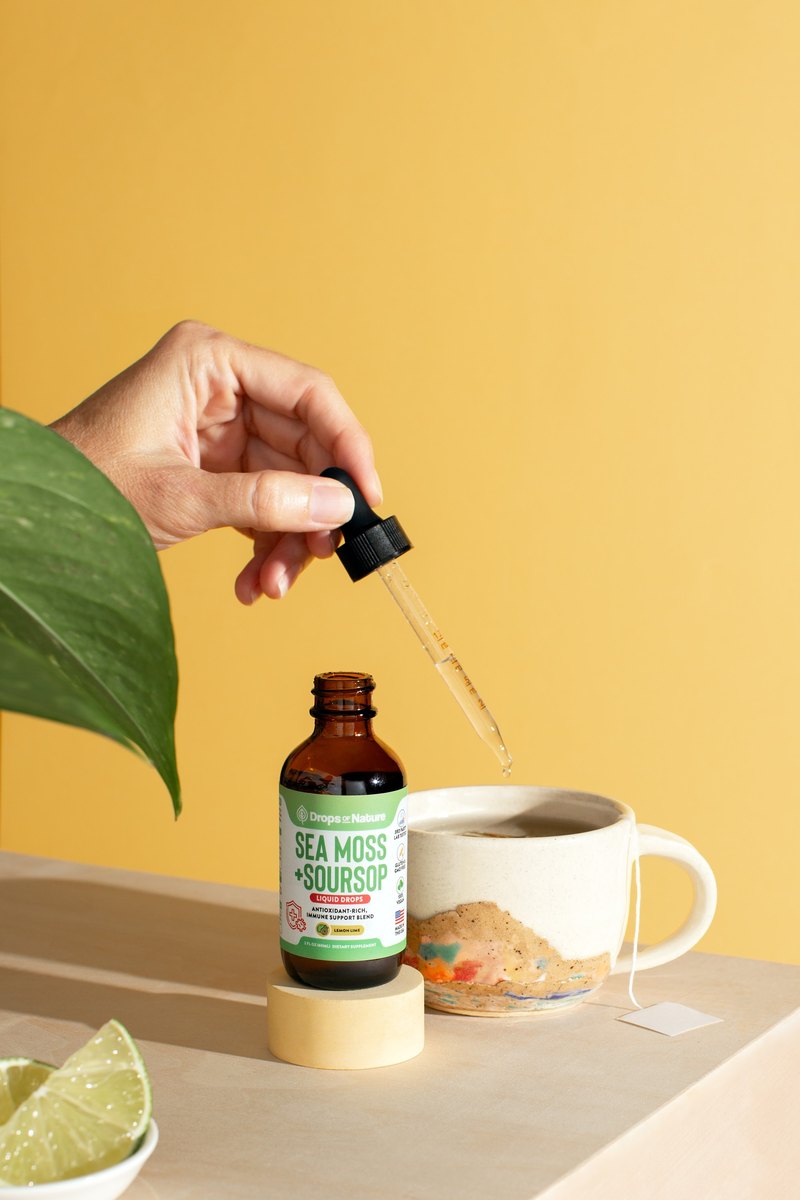 Soursop + Sea Moss drops beside a mug of tea with a lemon slice.