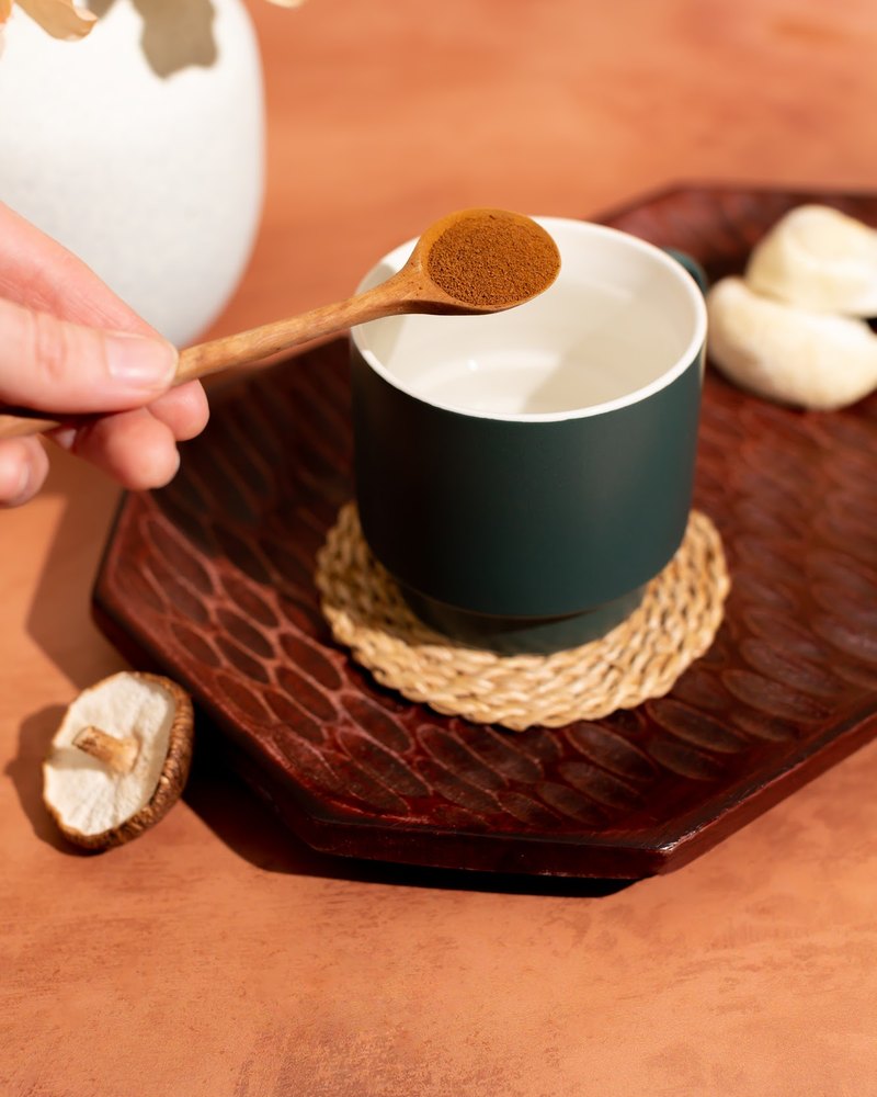 Hands spooning mushroom coffee into a mug in warm morning light
