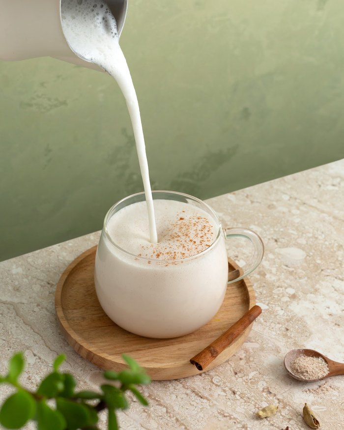 Steamed milk being poured into a glass of spiced chai on a wooden tray