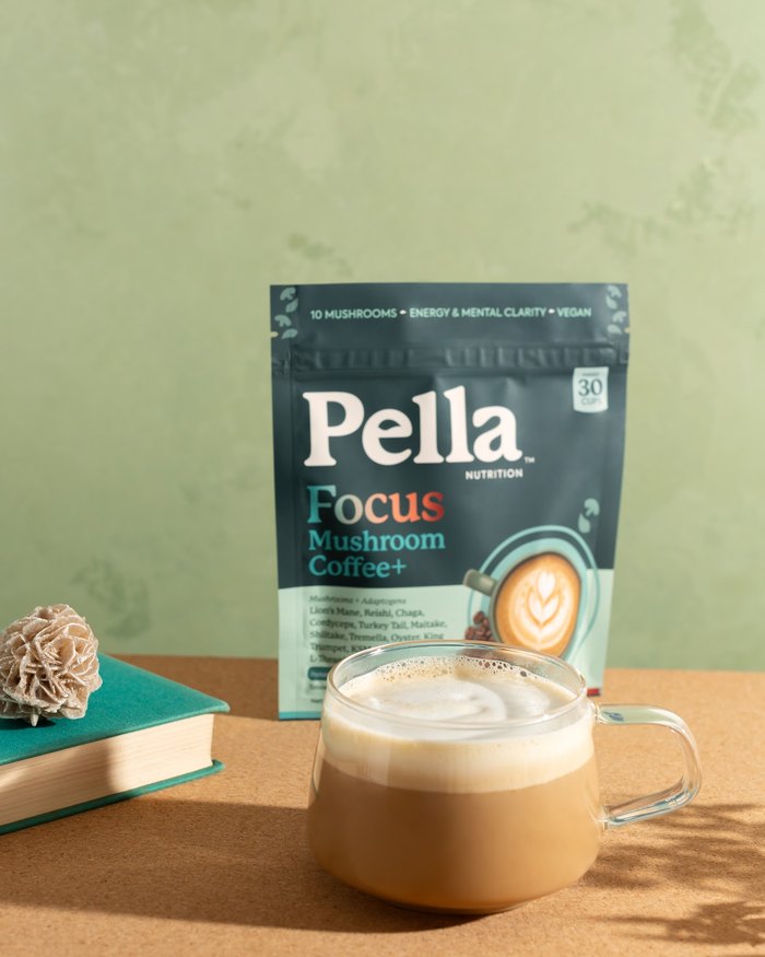 A frothy Focus coffee in a glass mug beside the Focus bag and a book