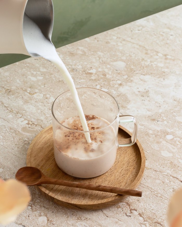 Milk being poured into a glass mug of mushroom hot chocolate on a wooden saucer