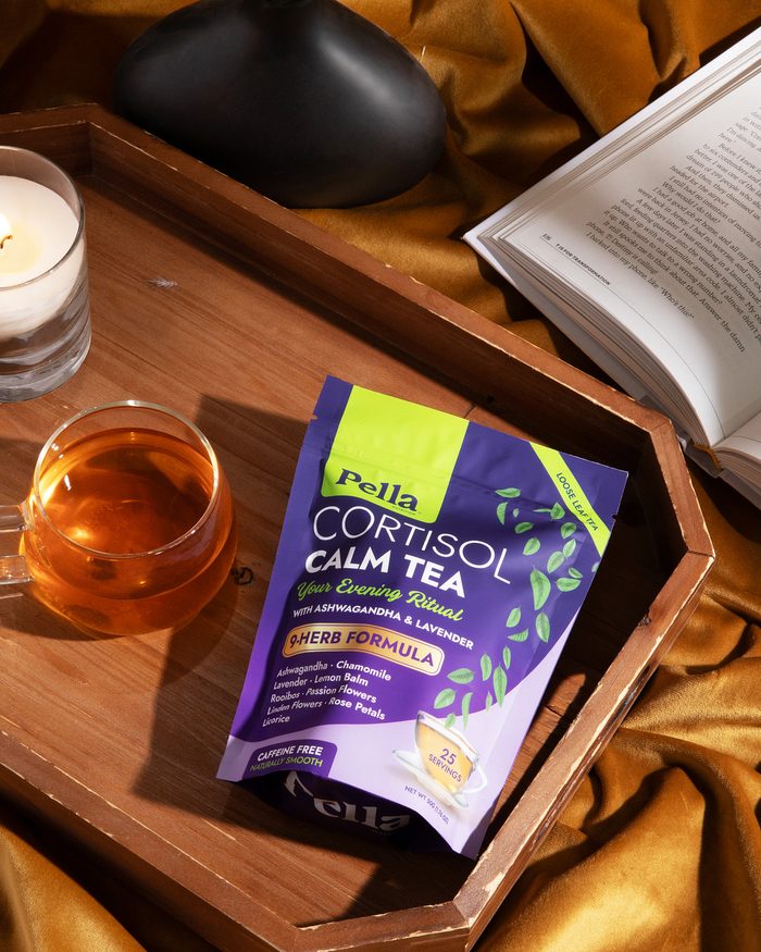 The Cortisol Calm tea pouch on a wooden tray with a glass of brewed tea, a candle and an open book