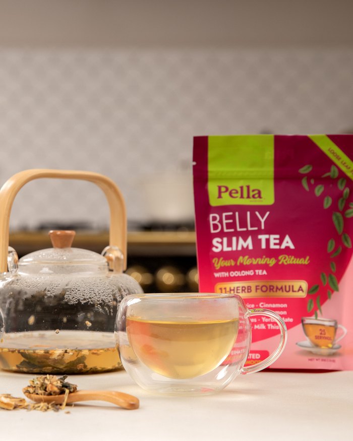 The Belly Slim tea pouch beside a glass teapot and a cup of brewed tea